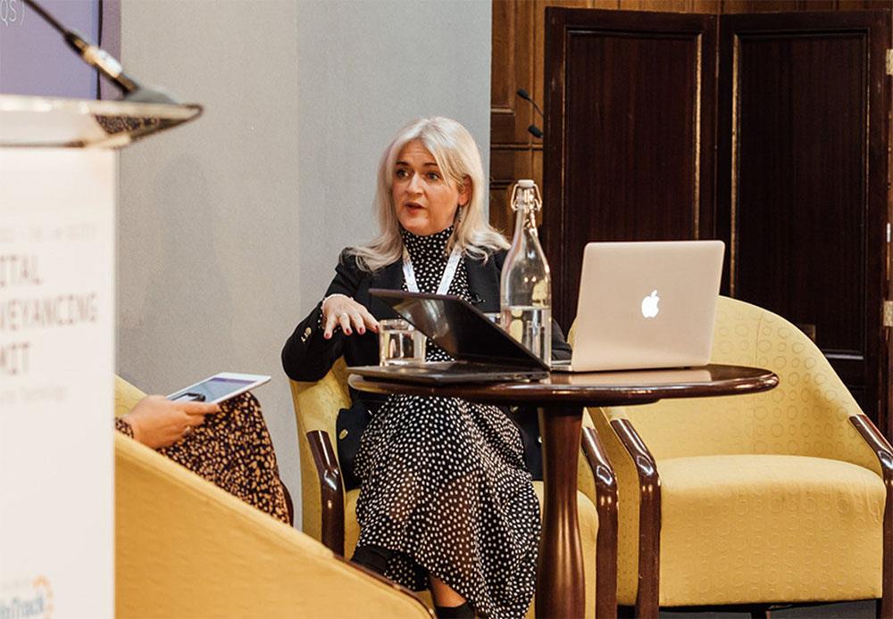 Tracy Thompson sitting on a yellow arm chair on stage at the digital conveyancing summit 2022